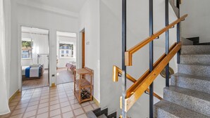 Un interior moderno con una escalera, un sillón de mimbre y una cama con una manta azul.