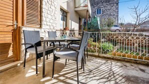 Un balcón al aire libre con una mesa y sillas, un muro de piedra y vistas a un edificio cercano.