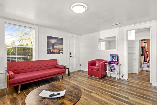 Un salón con un sofá rojo, una mesa de centro y un sillón rojo. Hay un cuadro en la pared y una mesita con una revista.