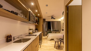 Eine moderne Küche mit Kochinsel, ein Essbereich mit hohem Tisch und Stühlen sowie ein Schlafzimmer mit großem Bett und Nachttisch.