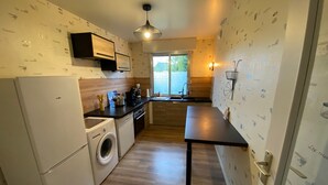 A compact kitchen with a washing machine, a coffee machine, and a dining table. - Apartment 'Le Lodge D Angèle' with Balcony and Wi-Fi (Honfleur)