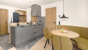 Een moderne keuken met grijze kastjes, een centraal eiland en een eetgedeelte met een ronde tafel en gele stoelen.