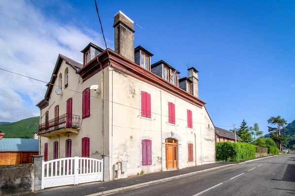 A two-story building with a balcony, a wooden door, and a white gate. - Au nid du gypaéte (oiseau local) (Bedous)