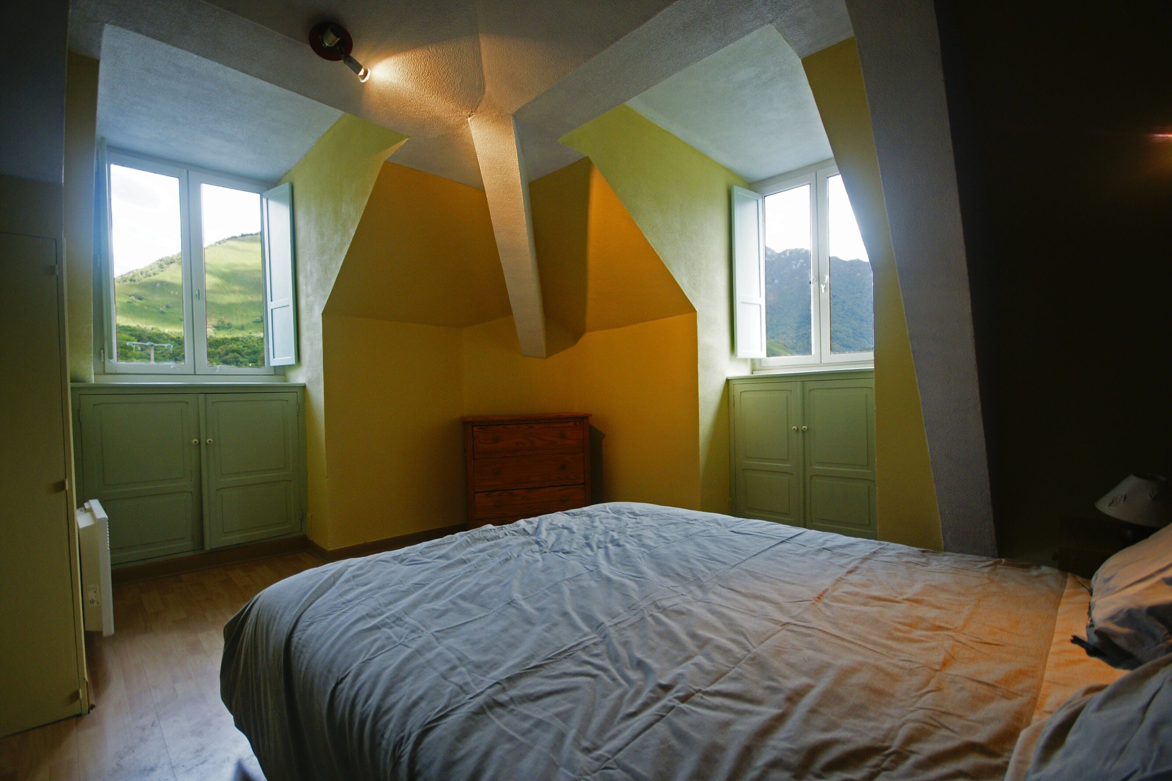 A bedroom with a bed, a dresser, and a window with a view of hills.