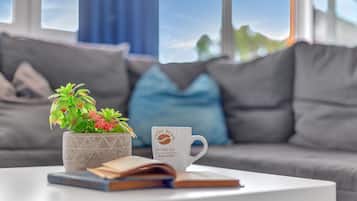 A modern living room with a white coffee table, a potted plant, a coffee mug, and an open book.