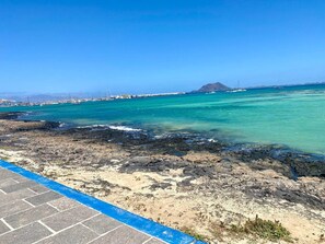 Une vue sur la côte, avec une eau turquoise et limpide, un rivage rocheux et des bâtiments qui se dessinent à l’horizon.