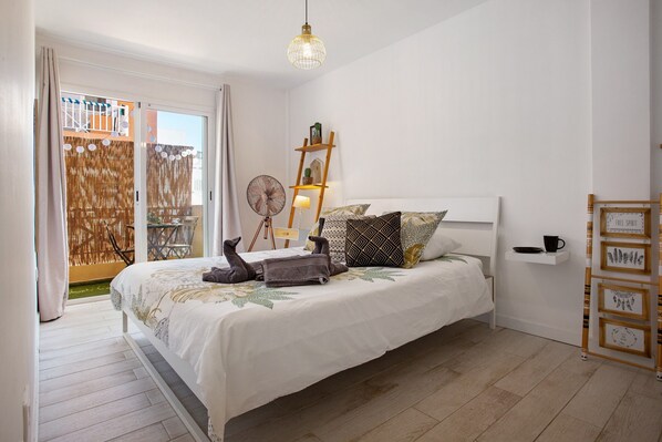 A bedroom with a bed, a ladder, a fan, and a shelf with framed pictures. - Vacation Apartment 'Corralejo Home Beach and Center' with Balcony and Wi-Fi (Corralejo)