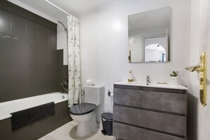 Une salle de bain comprenant une baignoire, des toilettes, un meuble-lavabo avec des tiroirs et un miroir.