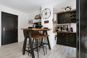 A kitchen with a dining table, bar stools, a clock, and a washing machine. - Vacation Apartment 'Corralejo Home Beach and Center' with Balcony and Wi-Fi (Corralejo)