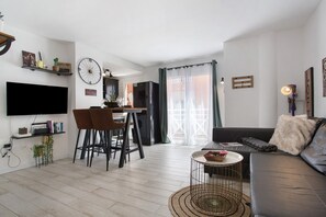 A modern living room with a flat-screen TV, a dining area with chairs, a sofa, and a small round table. - Vacation Apartment 'Corralejo Home Beach and Center' with Balcony and Wi-Fi (Corralejo)