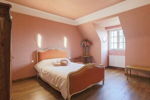 Ein Schlafzimmer mit einem Bett, einem kleinen Tisch, einem Sessel, einem Fenster und einer Heizung.