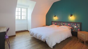 A bedroom with a bed, a nightstand, a chair, a window, and a wall with a floral headboard.