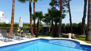 A swimming pool with lounge chairs and umbrellas, surrounded by tall palm trees and a clear sky. - Villa "Playa" with Mountain View, Private Pool & Wi-Fi (Pollensa)