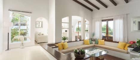 A spacious living room with a large sofa, a glass coffee table, and a view of the outdoors.