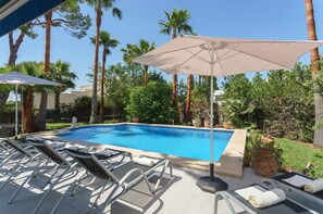 A swimming pool with lounge chairs and umbrellas, surrounded by palm trees and greenery. - Villa "Playa" with Mountain View, Private Pool & Wi-Fi (Pollensa)