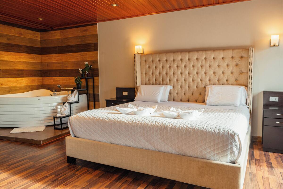 A spacious bedroom with a large bed, a separate sitting area with a bathtub, and a wooden ceiling.