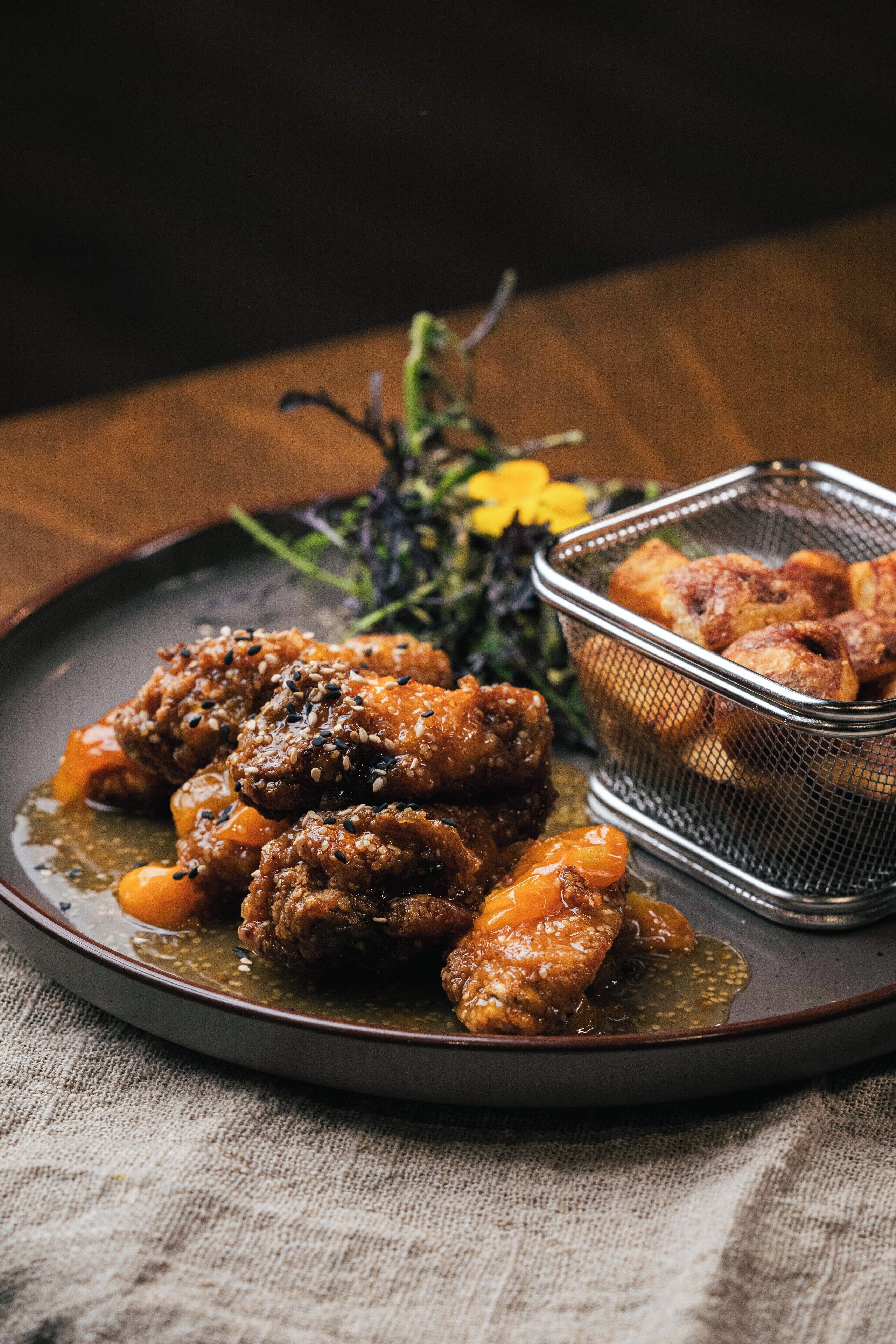 A plate of food with a metal basket containing fried items, set on a dark plate with a textured surface.