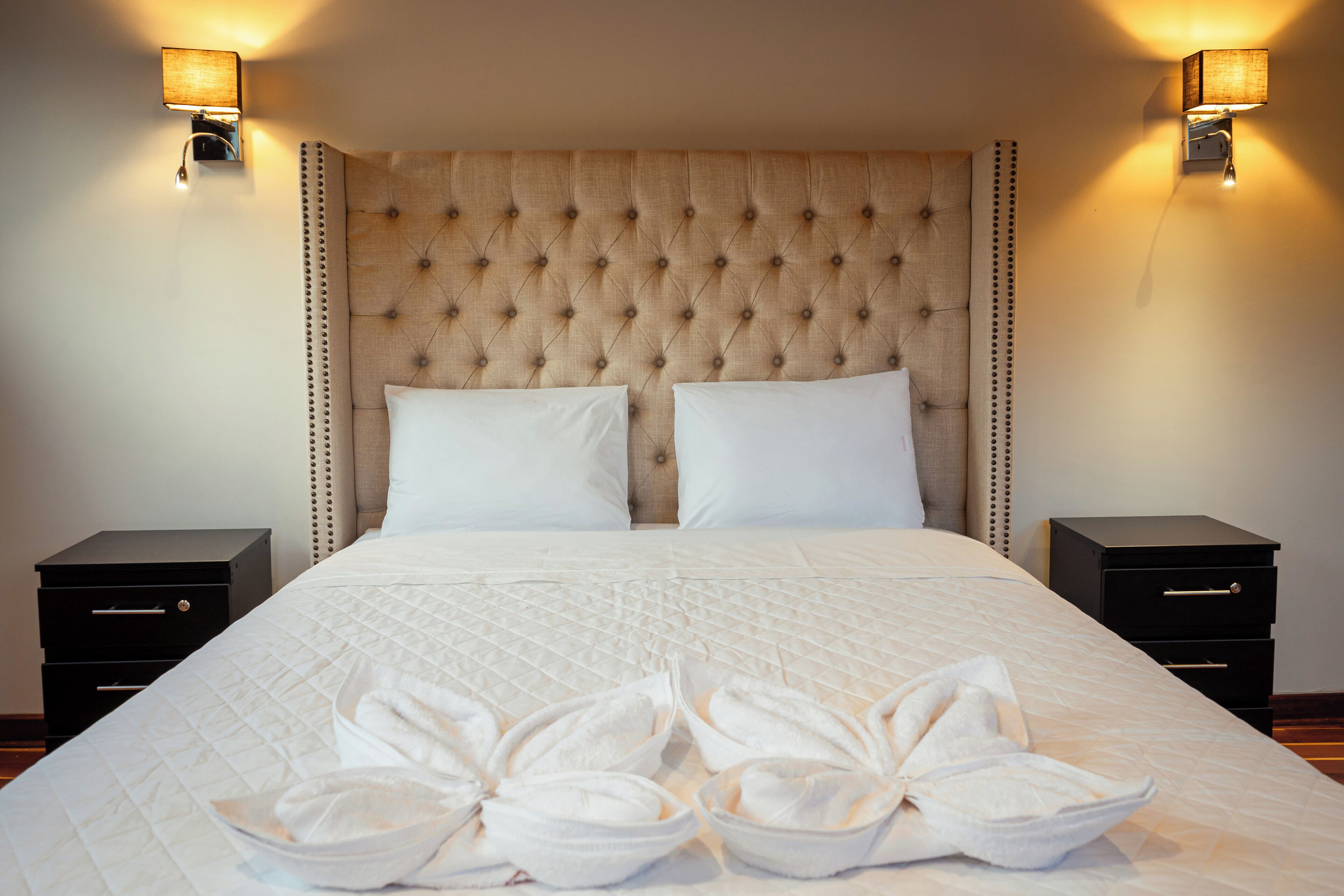 Una habitación de hotel con una cama grande, dos mesitas de noche y lámparas fijadas a la pared.