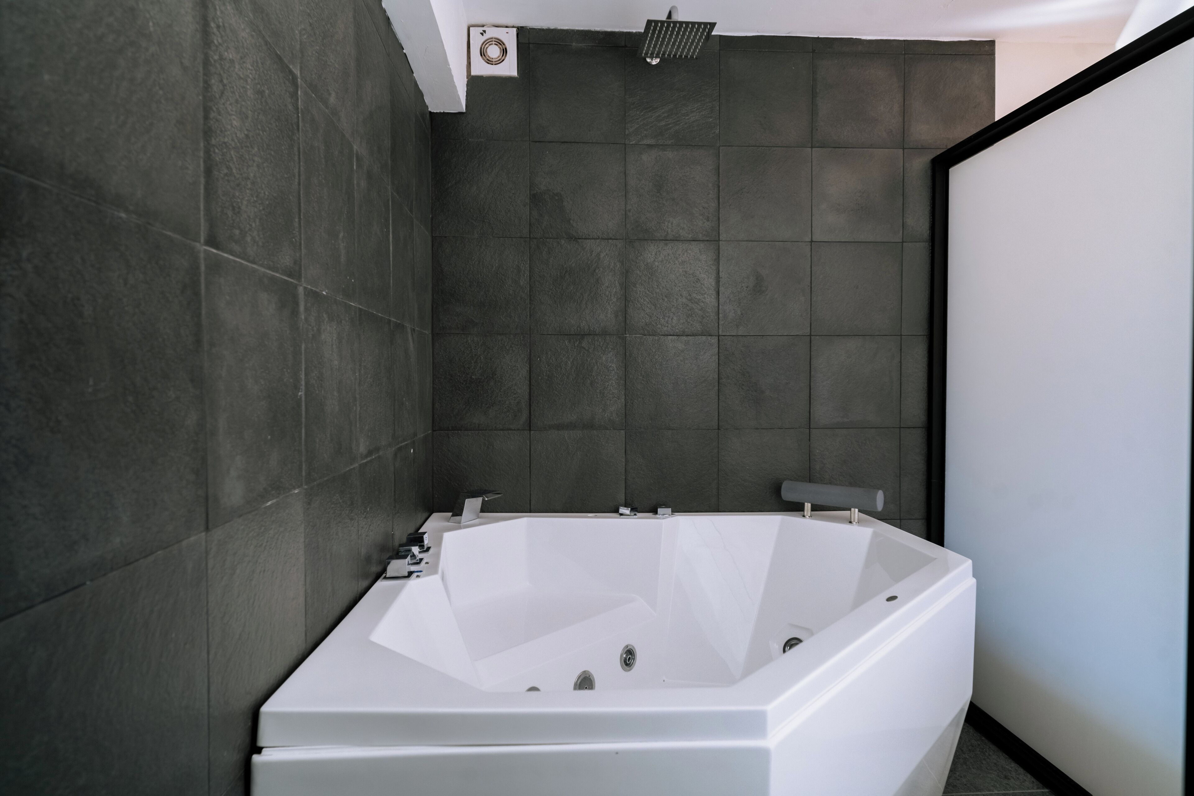 A modern bathroom with a freestanding bathtub, dark tiled walls, and a minimalist design.