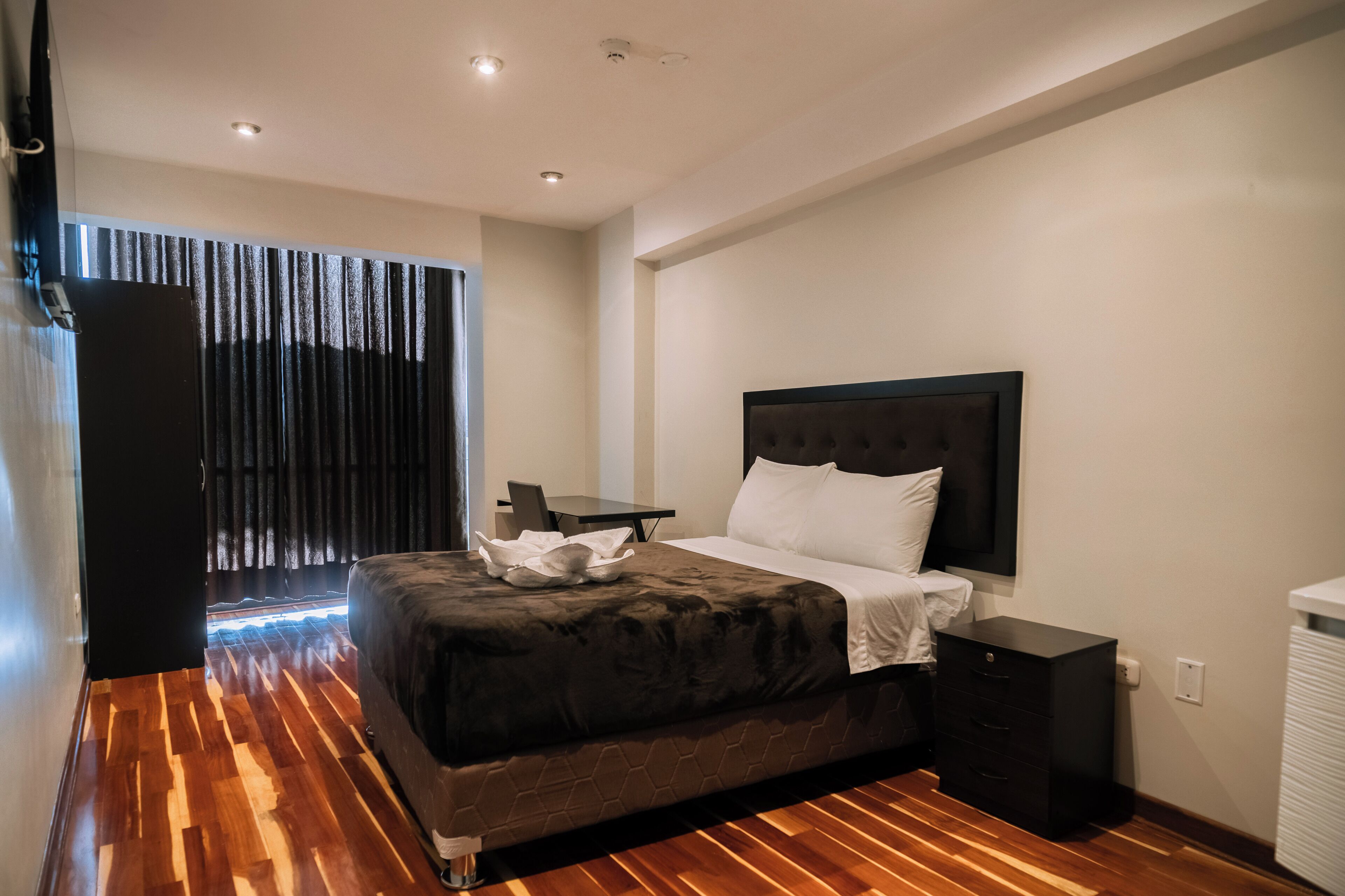 A modern hotel room with a large bed, a desk, and a wardrobe.