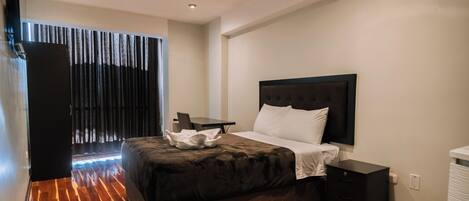 A modern hotel room with a large bed, a desk, and a wardrobe.