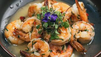 A bowl of cooked shrimp garnished with herbs and a purple flower, placed on a woven mat.