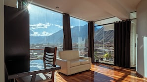 A modern living room with a sofa, a dining table, and a large window offering a mountain view. - Hotel California Urubamba (Urubamba)