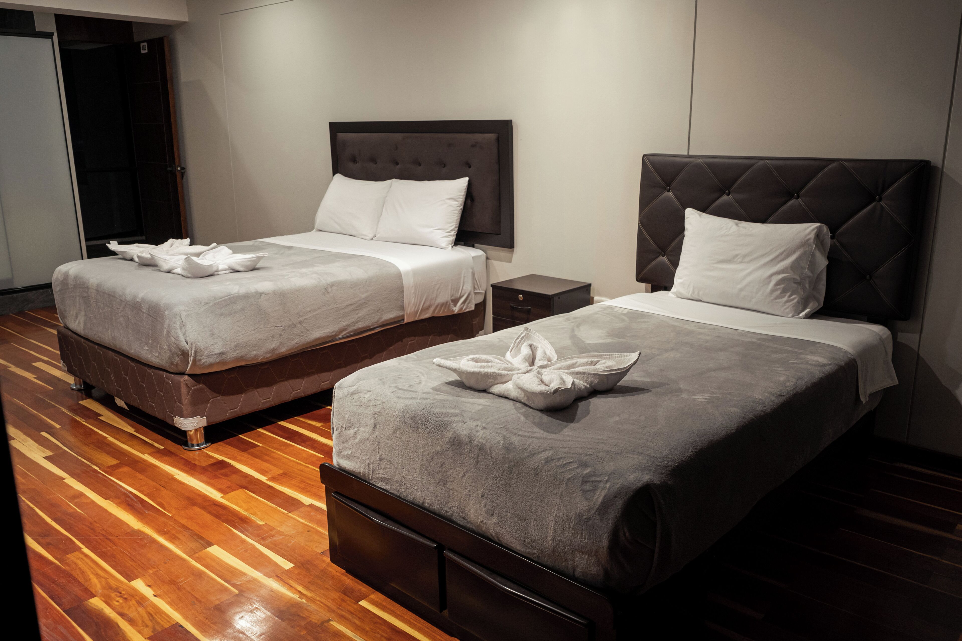 Two twin beds with dark headboards, white linens, and a wooden floor.