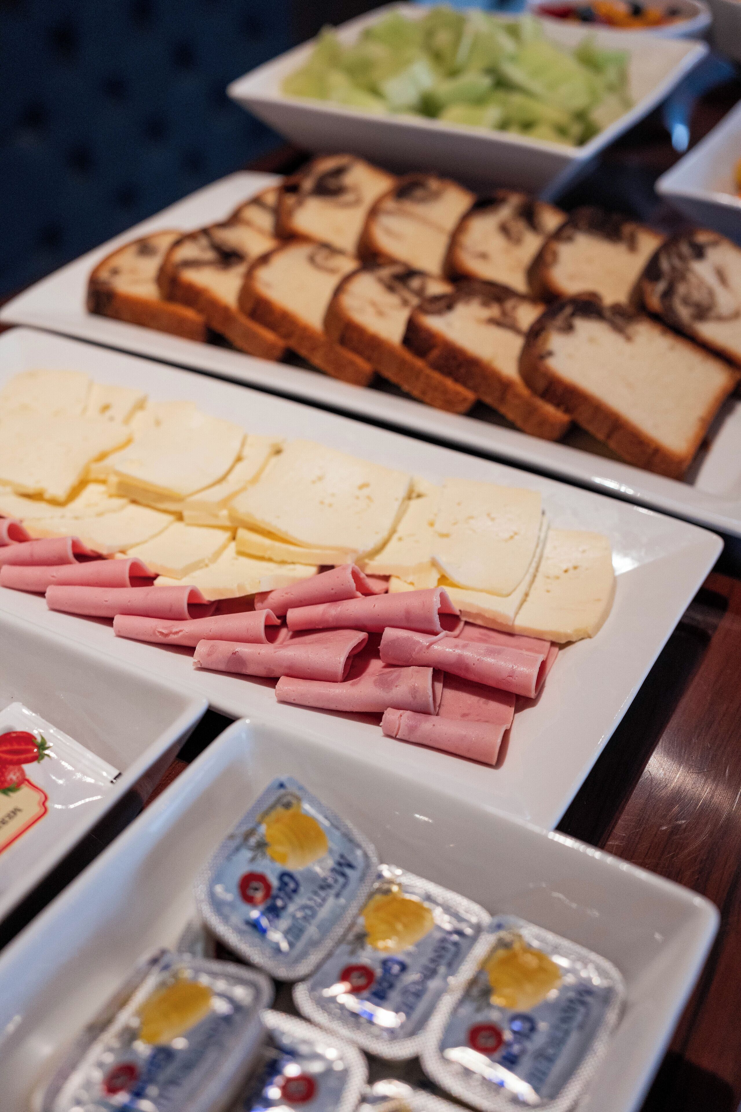 A buffet with various food items including sliced bread, cheese, ham, and butter.