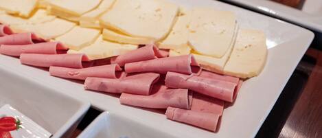 A buffet with various food items including sliced bread, cheese, ham, and butter.