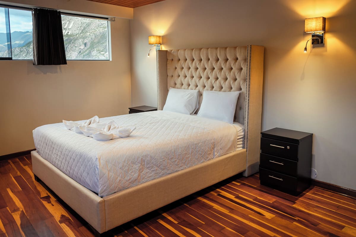 A neatly made bed with a quilted cover, a bedside table with a lamp, and a small filing cabinet.