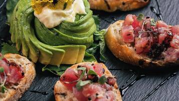 A variety of appetizers on a slate board, including avocado slices, a flower, and some bread with toppings.