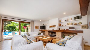 A living room with white sofas, a coffee table, and a fireplace. There is a pool visible through the glass doors. - Villa "Can Toni" with Mountain View, Private Pool & Wi-Fi (Pollensa)