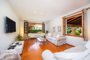 Una sala de estar moderna con un televisor de pantalla plana, un sofá, una mesa de centro y una ventana con vistas a la vegetación.