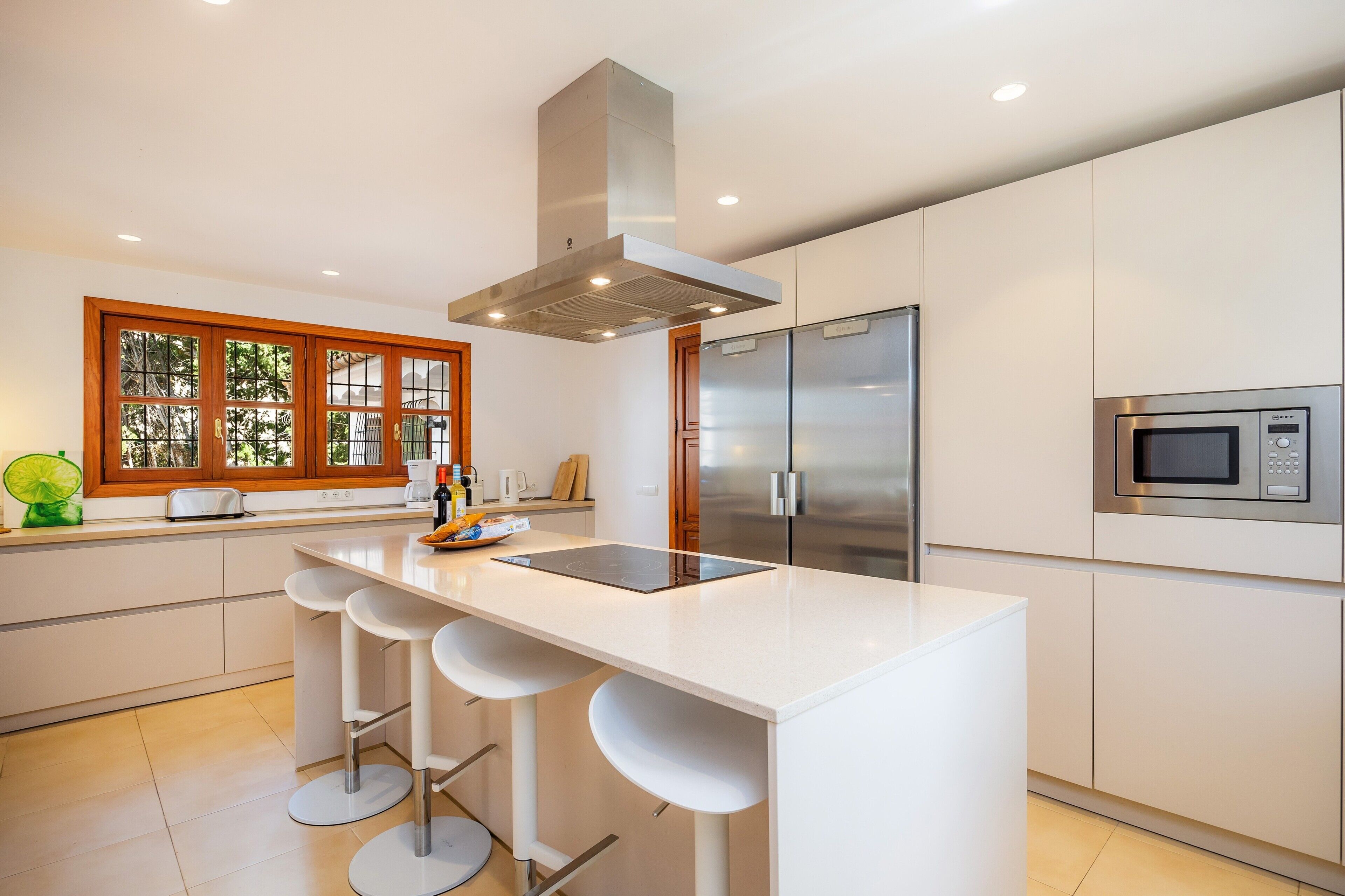 A modern kitchen with a central island, stainless steel appliances, and a window with wooden frames.