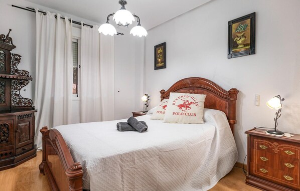 A bedroom with a wooden bed, white bedding, a nightstand with a lamp, a dresser, and a window with curtains. - Lovely apartment in Benalmádena (Benalmádena)