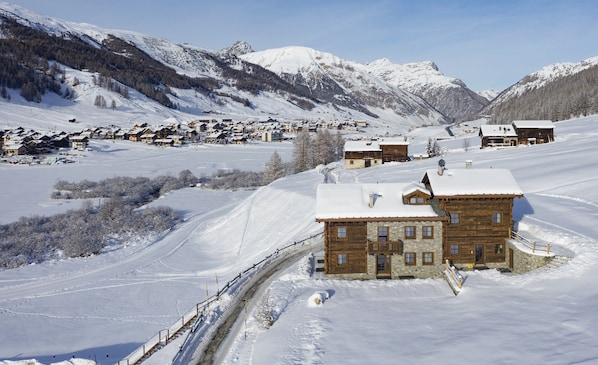 A snow-covered mountain village with wooden houses, a ski slope, and a clear sky. - Chalet 'Ice Villa Genf with Spa' with Mountain View, Shared Garden and Wi-Fi (Livigno)