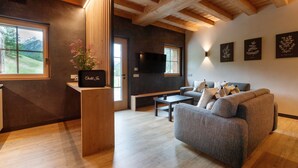 A modern living room with a sofa, a coffee table, a TV mounted on the wall, and a window with a view of mountains. - Chalet 'Ice Villa Genf with Spa' with Mountain View, Shared Garden and Wi-Fi (Livigno)