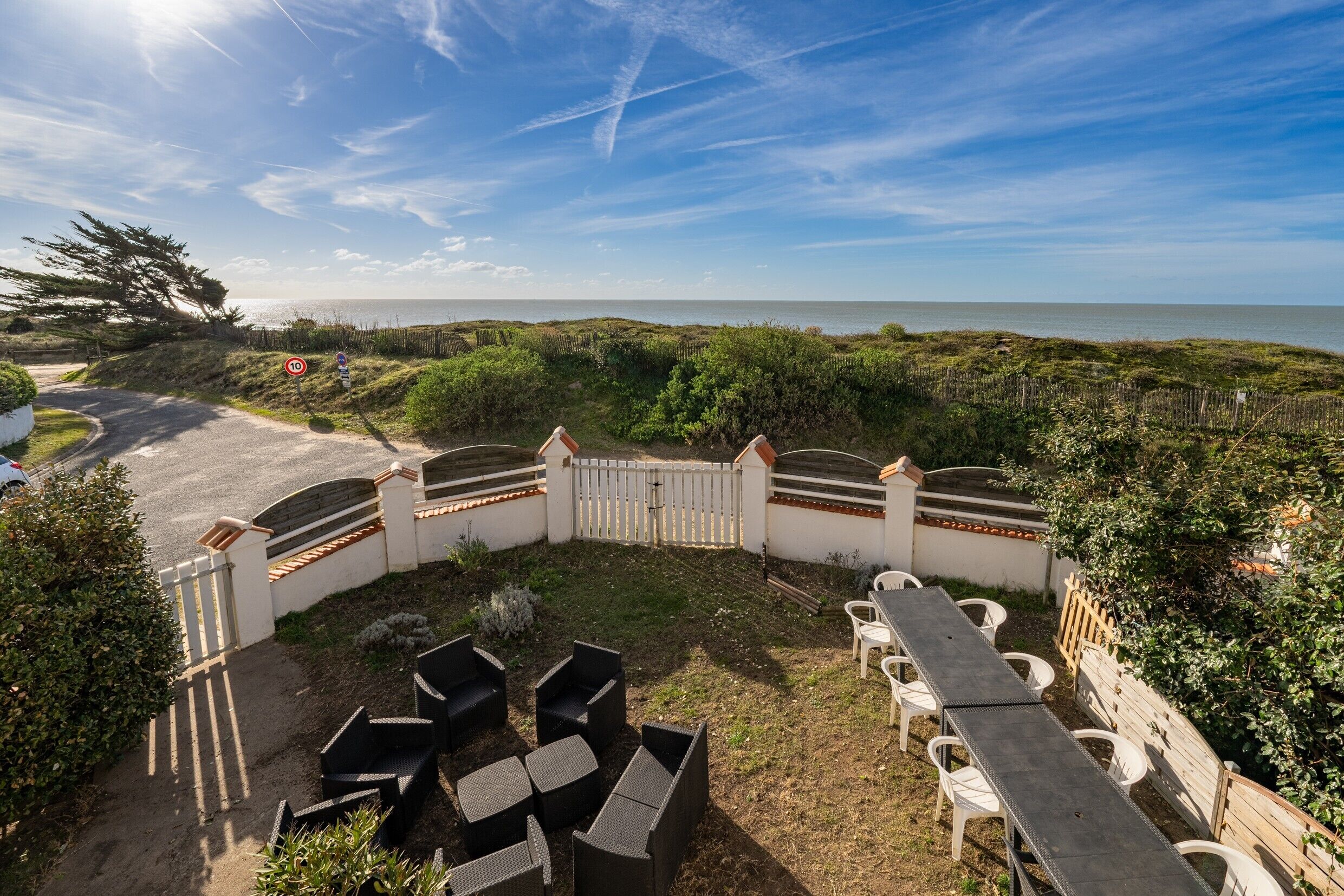 Eine Terrasse mit Sitzgelegenheit, Blick auf das Meer und einem weißen Zaun.