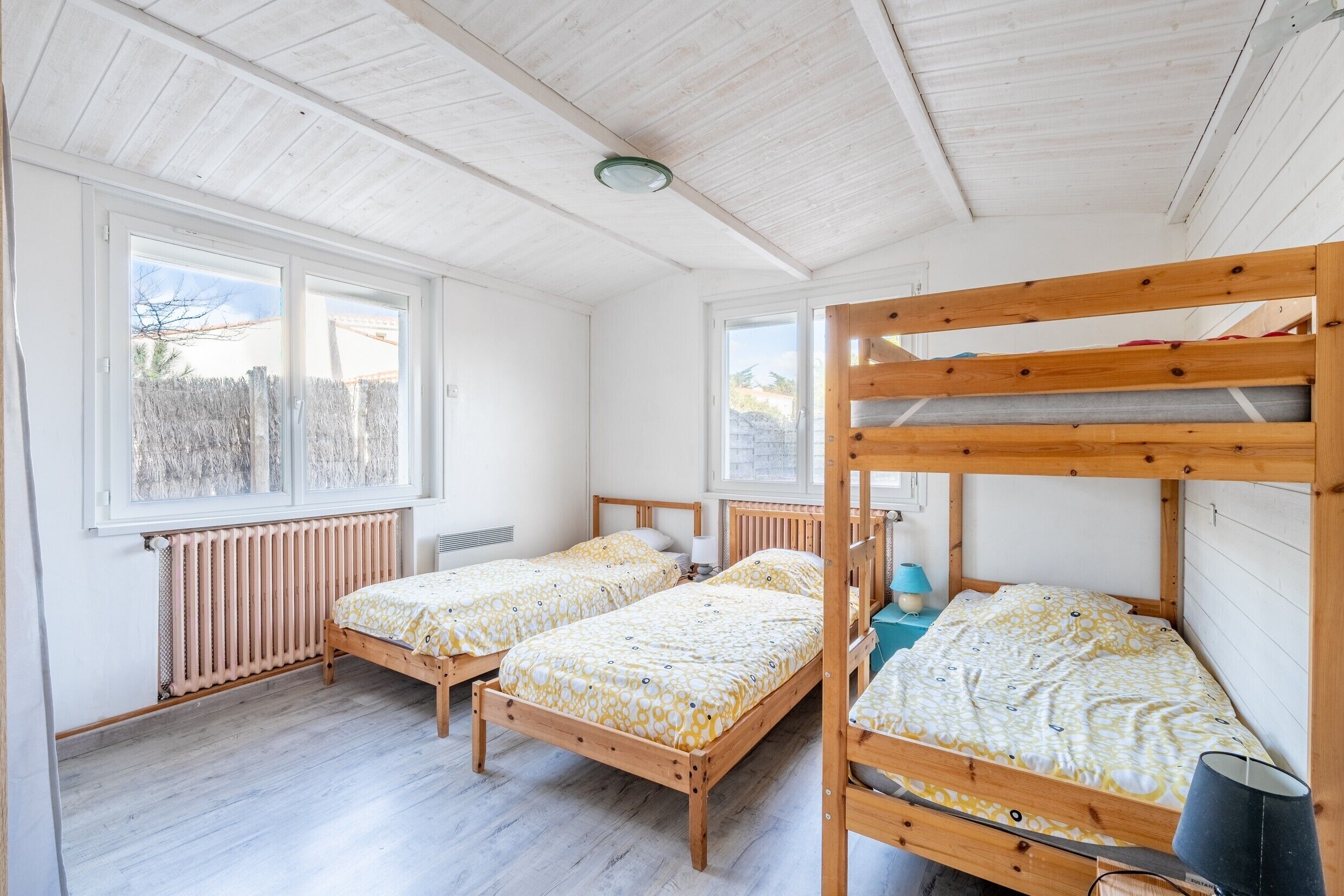 Quarto com duas camas de madeira, uma janela, um radiador e uma cama beliche.