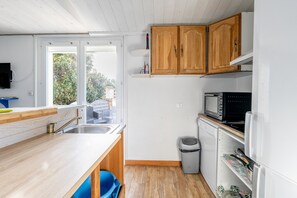 Une cuisine de taille réduite, dotée de meubles en bois, d’un four à micro-ondes, d’un évier et d’une poubelle.