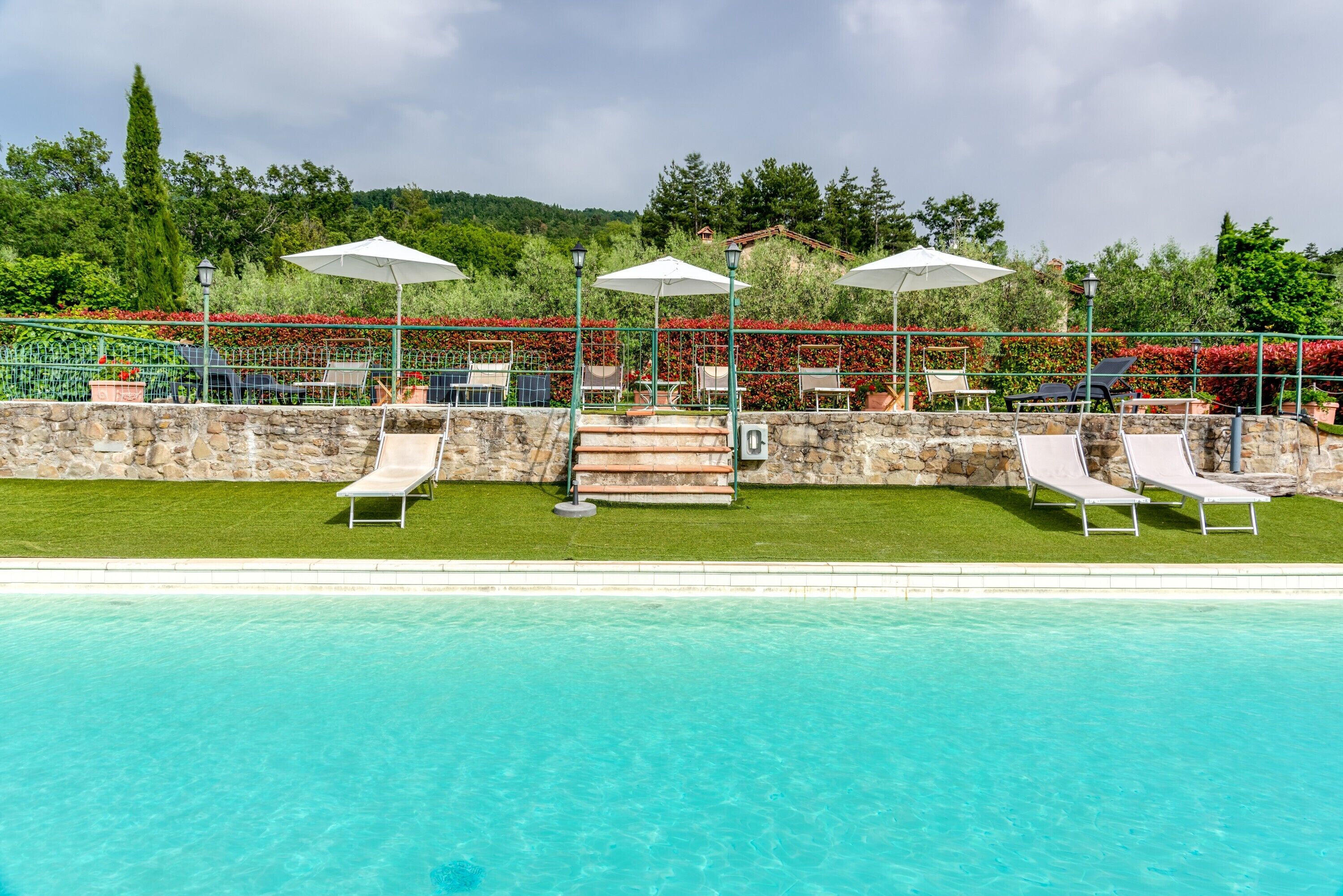 A poolside area with lounge chairs, umbrellas, and a stone wall.