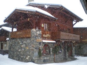 A stone building with a wooden balcony, surrounded by snow. - Apartment "Le Rhododendron" with Mountain Views, Shared Garden & Wi-Fi (La Plagne-Tarentaise)