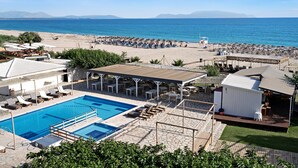 Et poolområde med liggestole, et overdækket siddeområde og udsigt til strand og hav.