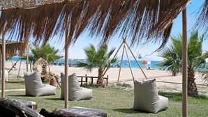 En strandloungeseng med liggestole, en stråparasol og udsigt til stranden og havet.