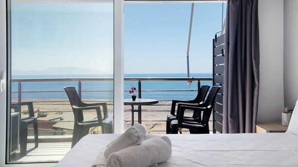 Et hotelværelse med seng, udsigt til stranden og en balkon med stole og bord.
