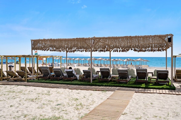 A beachside lounge area with wooden loungers, a thatched canopy, and a wooden deck leading to the beach.