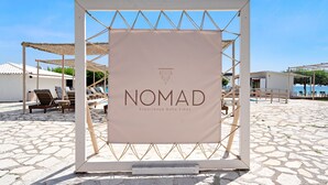 Et strandområde med et skilt der siger 'NOMAD Experience Boho Vibes' og udendørs siddepladser.