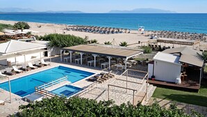 Et poolområde med liggestole, en lille pool og udsigt til stranden og havet.