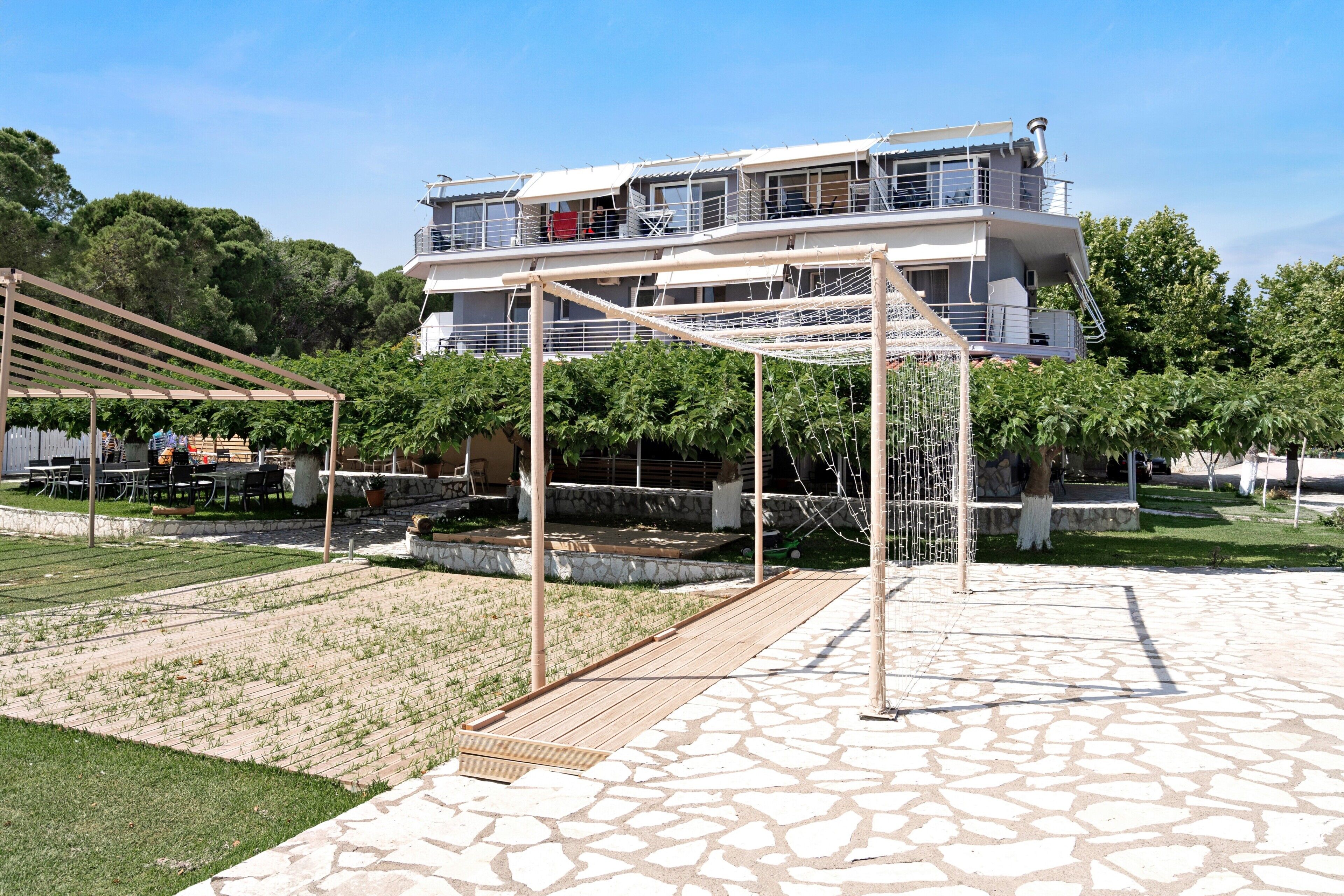 Ein mehrstöckiges Gebäude mit Dachterrasse, einer Pergola und einer gepflasterten Fläche mit Gras und Pflanzen.